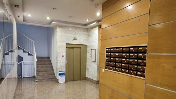 Un couloir avec un mur en bois, une poubelle, une porte et un escalier.