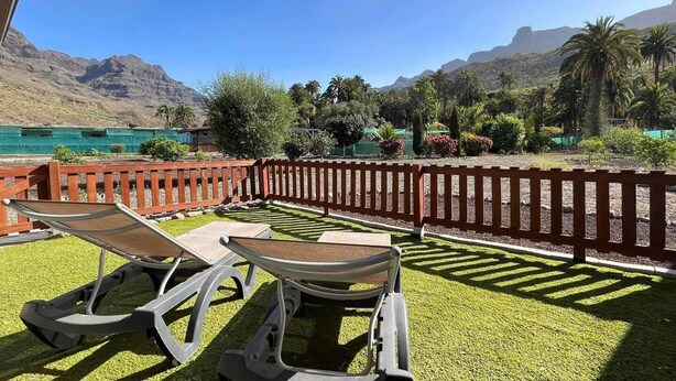 A patio with two lounge chairs and a table, overlooking a mountainous landscape with a pool and greenery. - Cosy Apartment in the Mountains Near Maspalomas (San Bartolomé de Tirajana)