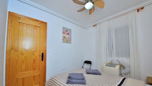 Ein Schlafzimmer mit Holztür, einem Bett mit gestreifter Bettwäsche, einem Deckenventilator und einem Fenster mit Vorhängen.