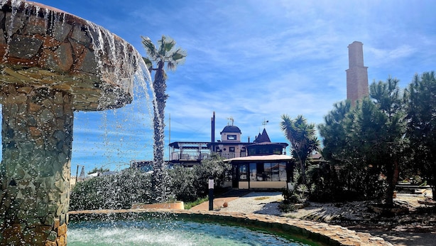 A stone fountain, a pool, and a building with a tower in the background. - Lovely Apartment Near the Beach in Sunny La Mata (Torrevieja)