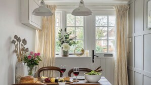Un comedor con una mesa dispuesta para dos, con un jarrón de flores, un bol de ensalada y una hogaza de pan.