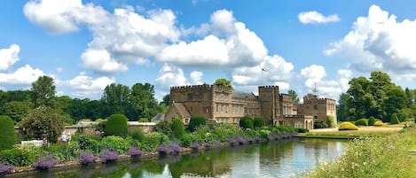 A historic building with a moat, surrounded by lush greenery and a clear sky.