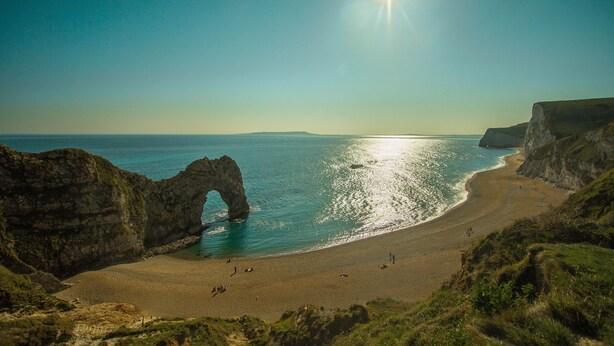 Un paisaje costero con un arco de roca natural, una playa arenosa y acantilados.