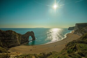 Un paisaje costero con un arco de roca natural, una playa arenosa y acantilados.