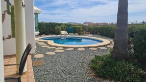Une piscine bordée de pierres, un palmier et une vue sur des collines lointaines.