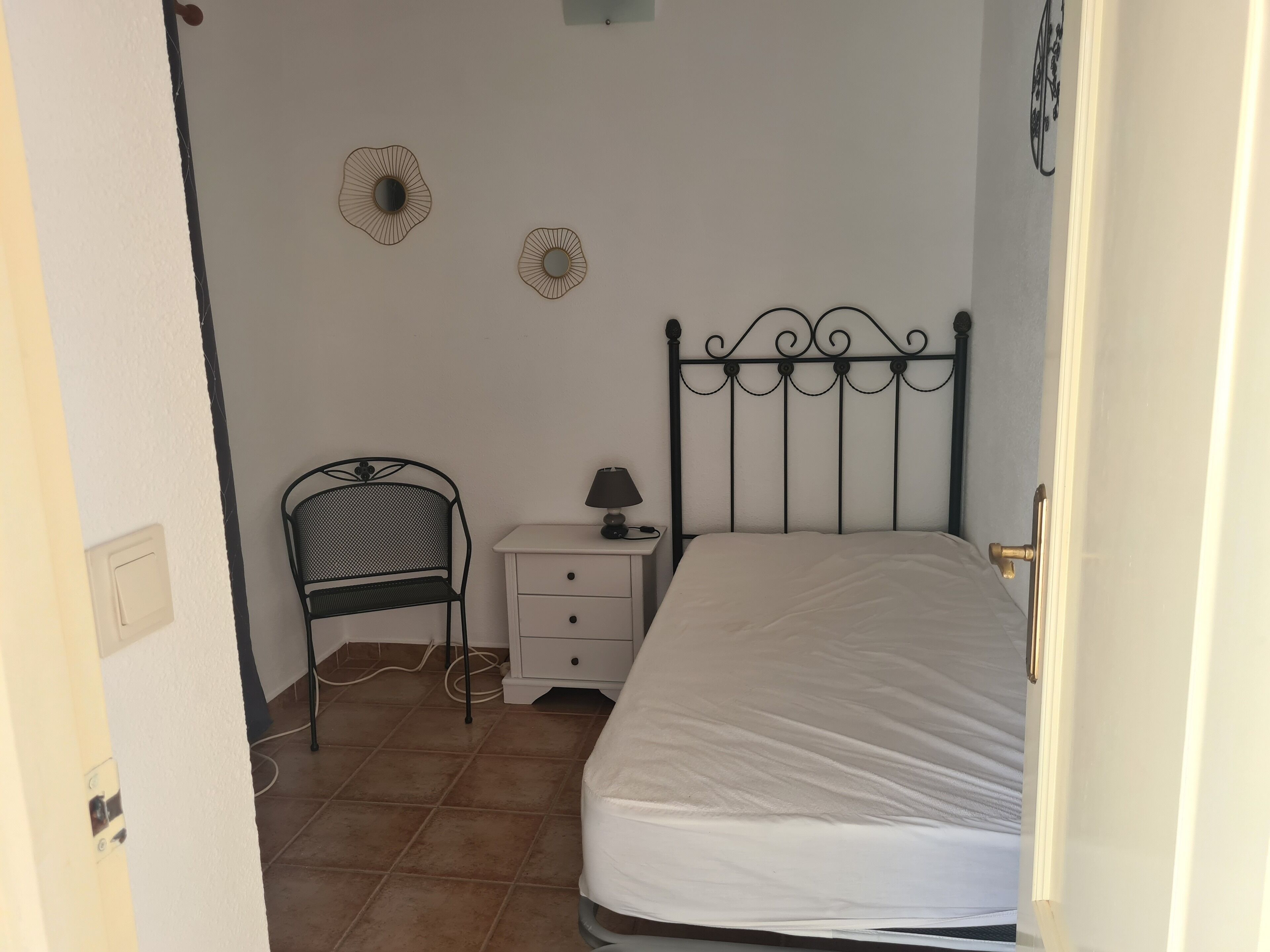 Une chambre à coucher avec un lit en métal, une table de chevet avec une lampe, une chaise et deux éléments de décoration murale.