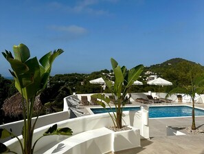 A rooftop pool area with lounge chairs and umbrellas, surrounded by tropical plants and overlooking a hillside. - Charming 1-bed Apartment (Javea)