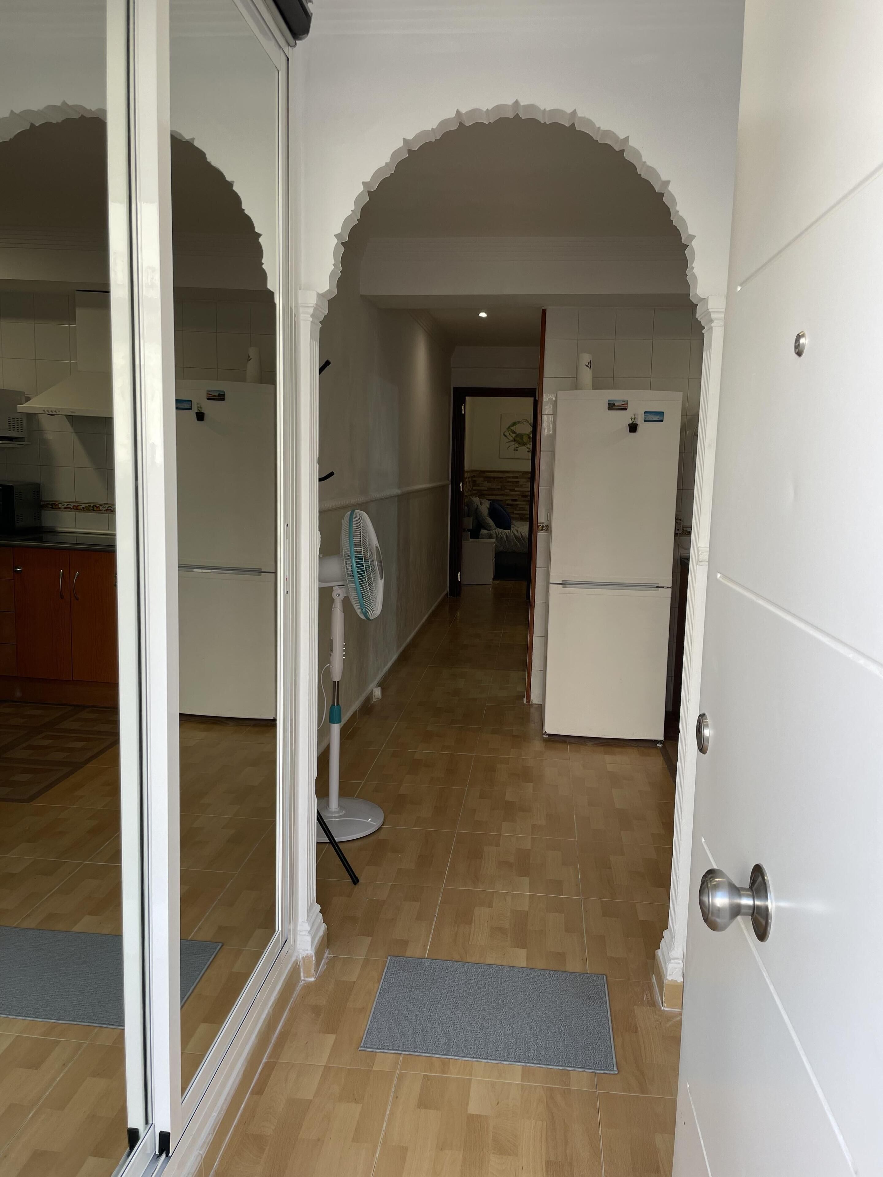A narrow hallway with white walls, wooden flooring, and a white door on the right.