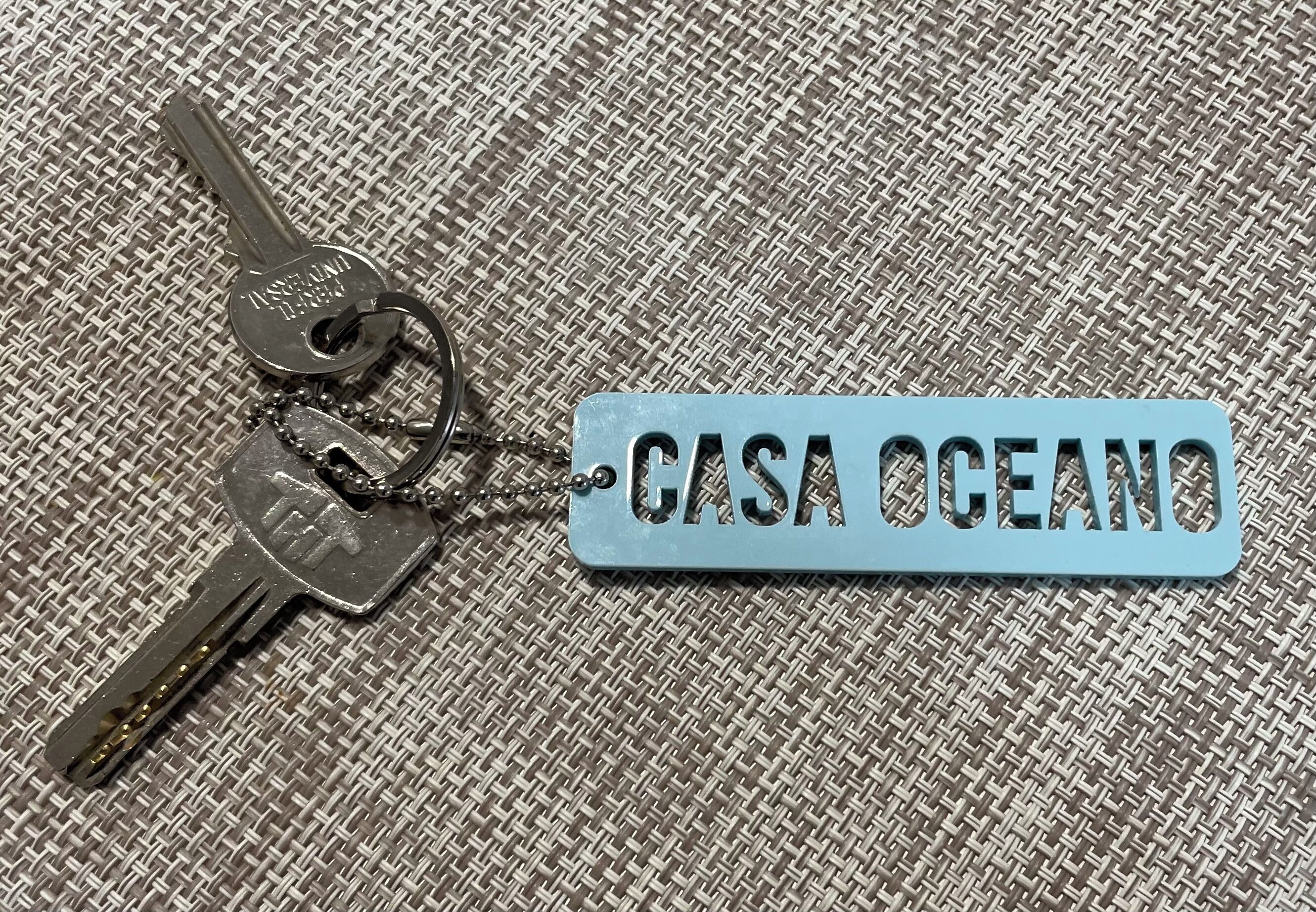 Un porte-clés avec une clé en métal et une étiquette bleue portant l’inscription « CASA OCEANO ».