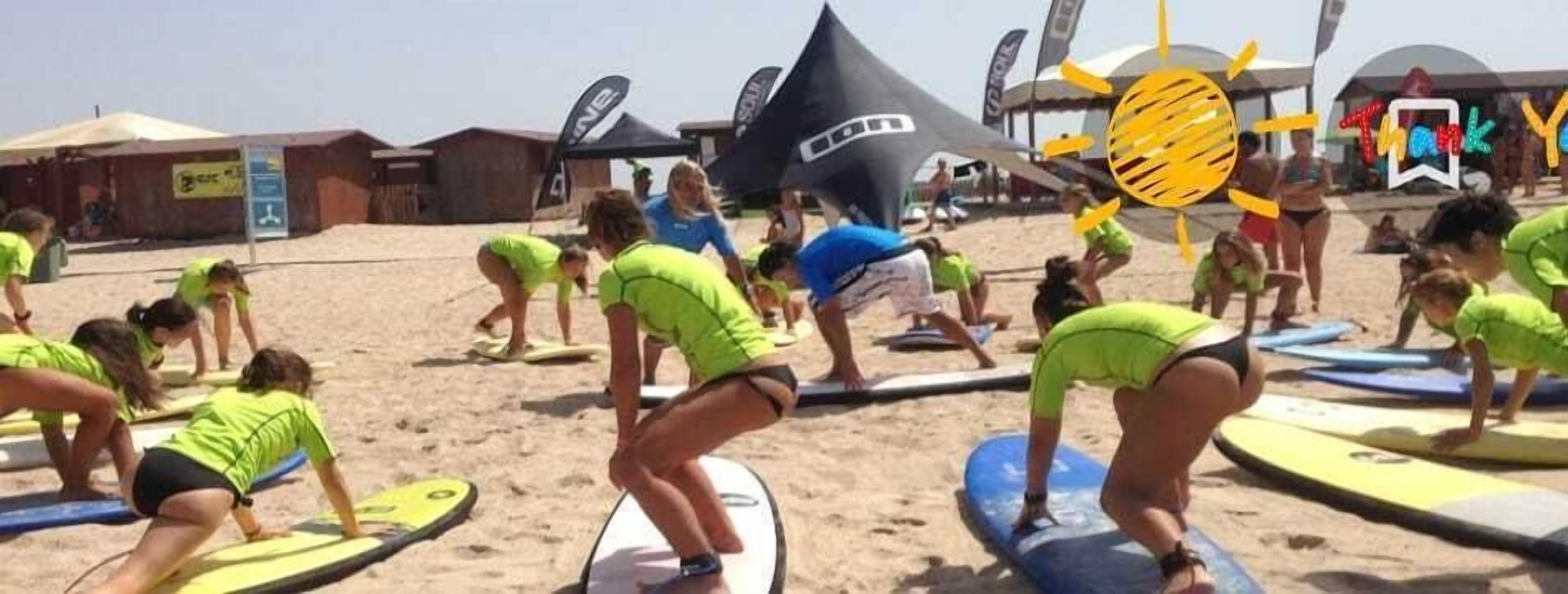 Un groupe de personnes sur une plage, avec des planches de surf, des tentes et des drapeaux en arrière-plan.