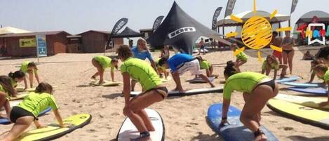 Un groupe de personnes sur une plage, avec des planches de surf, des tentes et des drapeaux en arrière-plan.