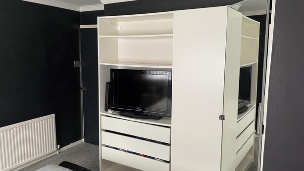 A room with a white built-in TV stand, a black TV, and a white bed. - A real homely home close to Gatwick and the South East of England. (Crawley)