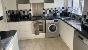A compact kitchen with white cabinets, a black countertop, a stainless steel range hood, a built-in dishwasher, and a window with a view. - A real homely home close to Gatwick and the South East of England. (Crawley)