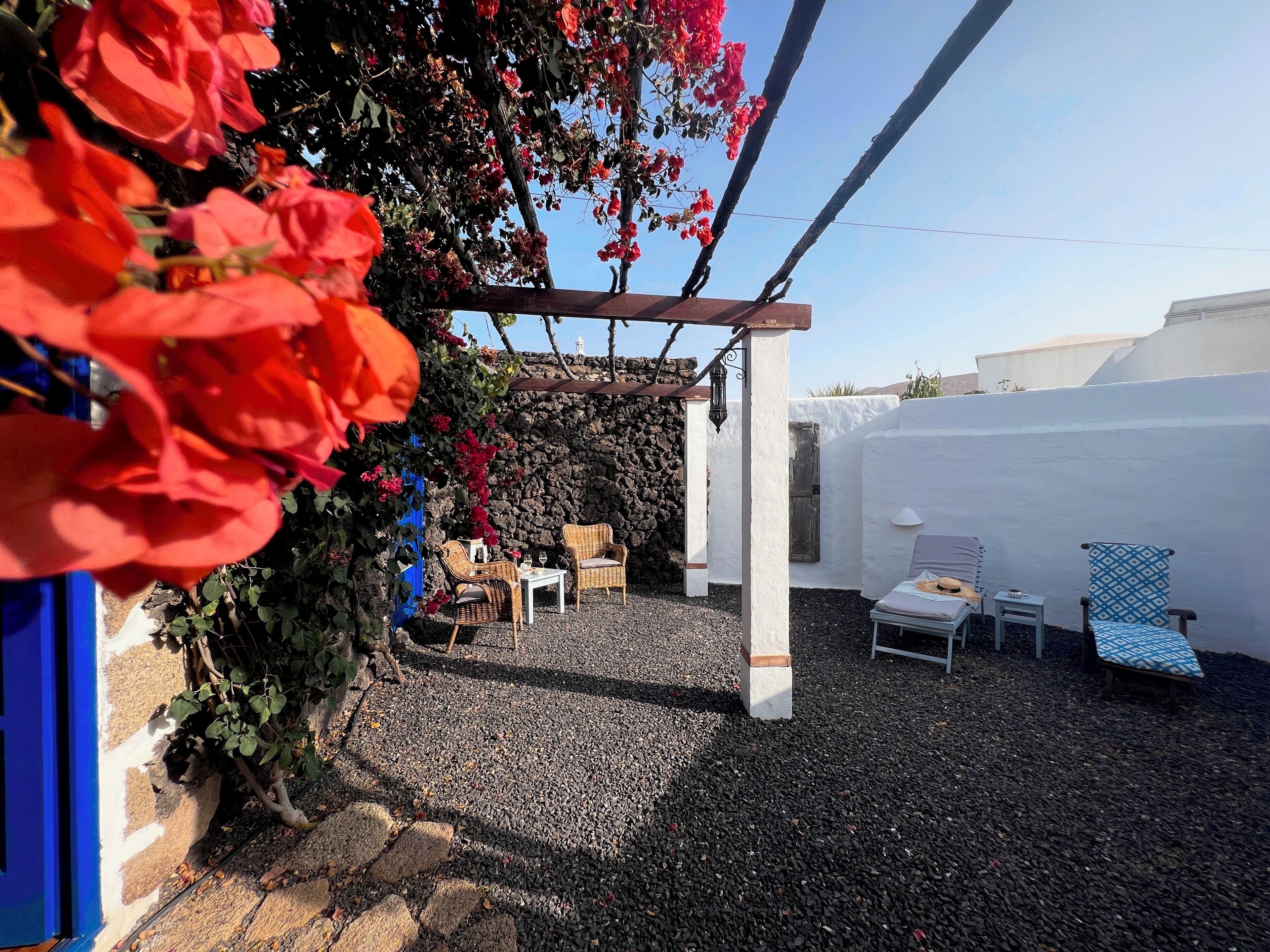 A patio area with wicker furniture, a white wall, and a stone wall in the background.