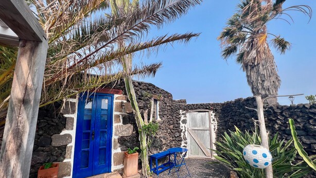 Un bâtiment aux murs de pierre, avec une porte bleue et un petit banc bleu.