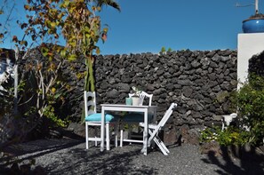 A white outdoor seating area with a table and chairs, a stone wall in the background, and some greenery. - Finca/privategardens/doublebed/freep/tv/wifi (Yaiza)