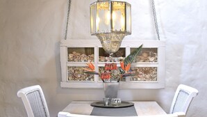 Une table à manger agrémentée d’une lampe décorative, de deux chaises et d’une fenêtre donnant sur une collection de coquillages.