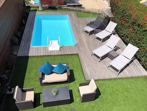 Piscina retangular com um deck de madeira ao redor, equipada com espreguiçadeiras e uma pequena mesa.