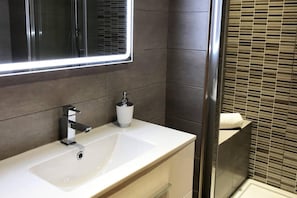 Casa de banho moderna com lavatório branco, espelho, dispensador de sabonete e suporte para toalhas.