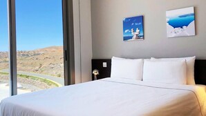 A hotel room with a large bed, two wall-mounted paintings, and a view of a coastal landscape through a large window. - Amazing Sunset Golf-course Villa for up to 7 (San Bartolomé de Tirajana)