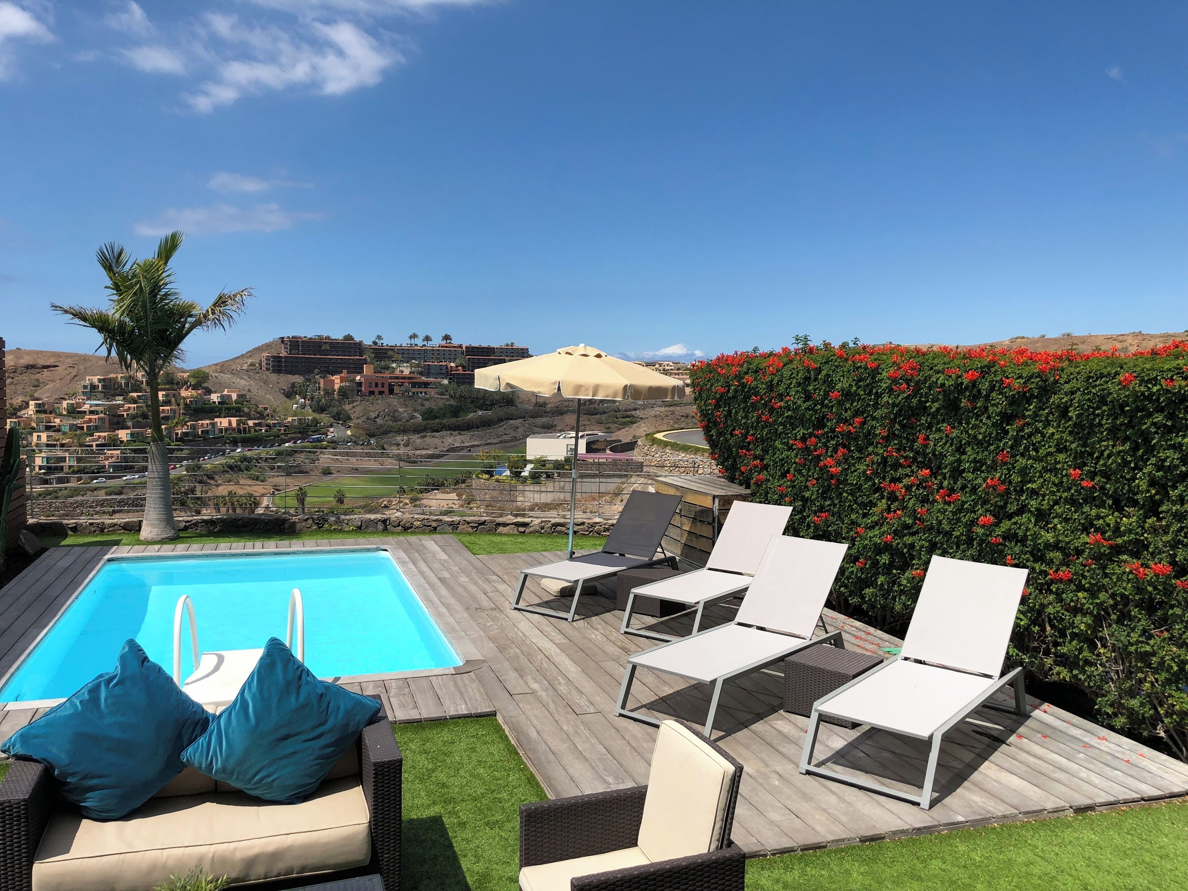 A poolside area with lounge chairs, a small pool, and a view of a hillside residential area.