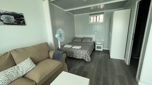 Une chambre à coucher de taille réduite, comprenant un lit, une table de chevet, une chaise, un ventilateur et une petite table.