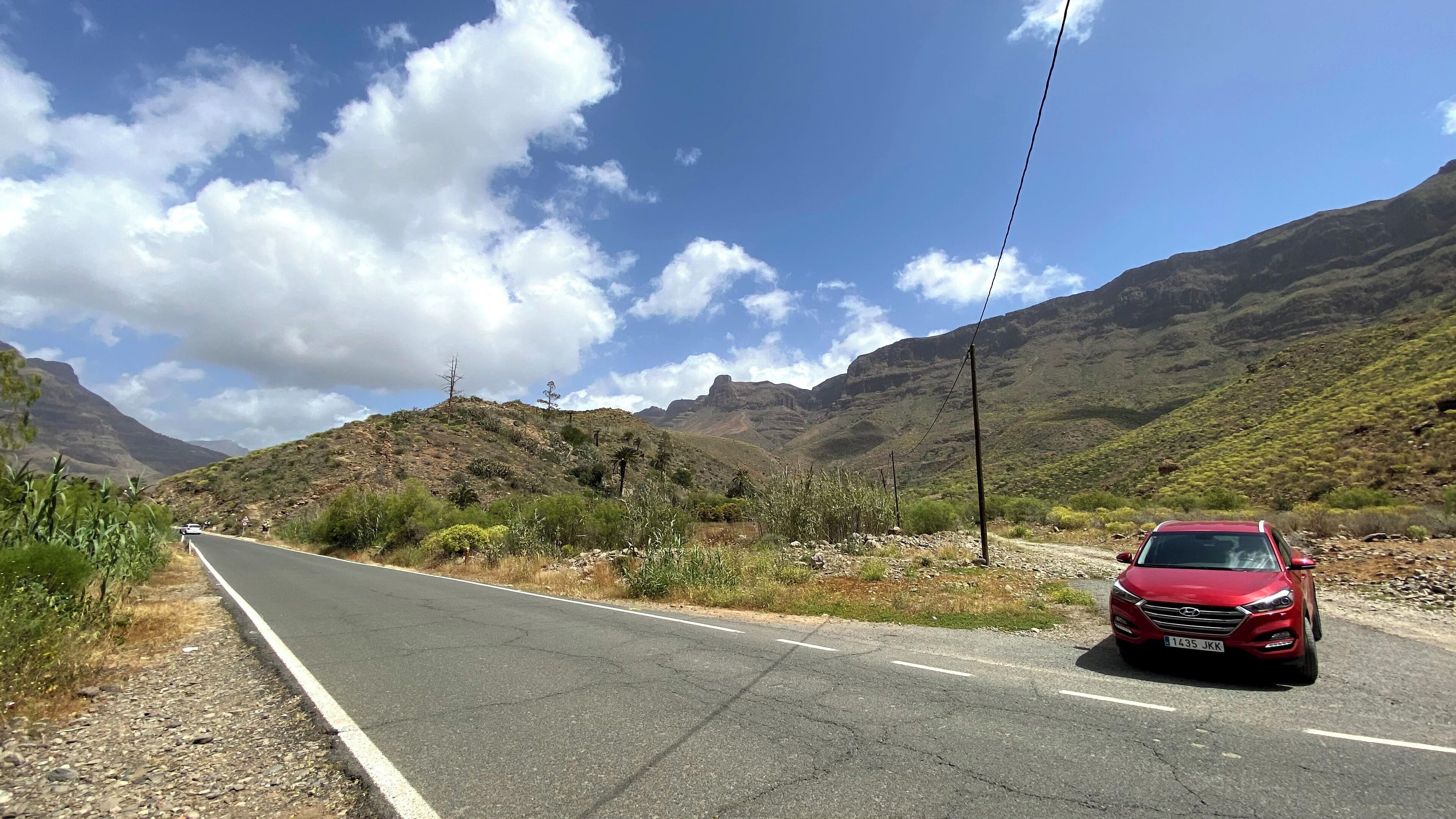 Un coche rojo en una carretera de dos carriles con montañas al fondo.
