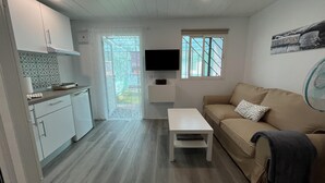 A compact living space with a kitchenette, a sofa, a small table, and a TV mounted on the wall. - Renovated Tiny House in the Country Near Fataga (San Bartolomé de Tirajana)