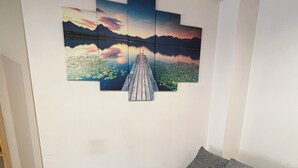 Ein Zimmer mit grauem Schlafsofa, Holzboden und einem Wandbild, das einen Sonnenuntergang über einem See mit Bergen zeigt.
