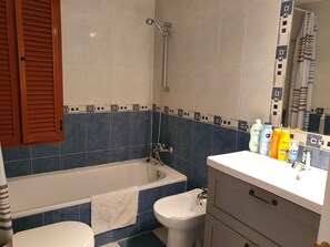A bathroom with a bathtub, a bidet, and a toilet. There are toiletries on the counter.