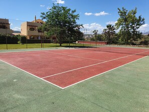 A tennis court with a net, surrounded by a fence and trees.