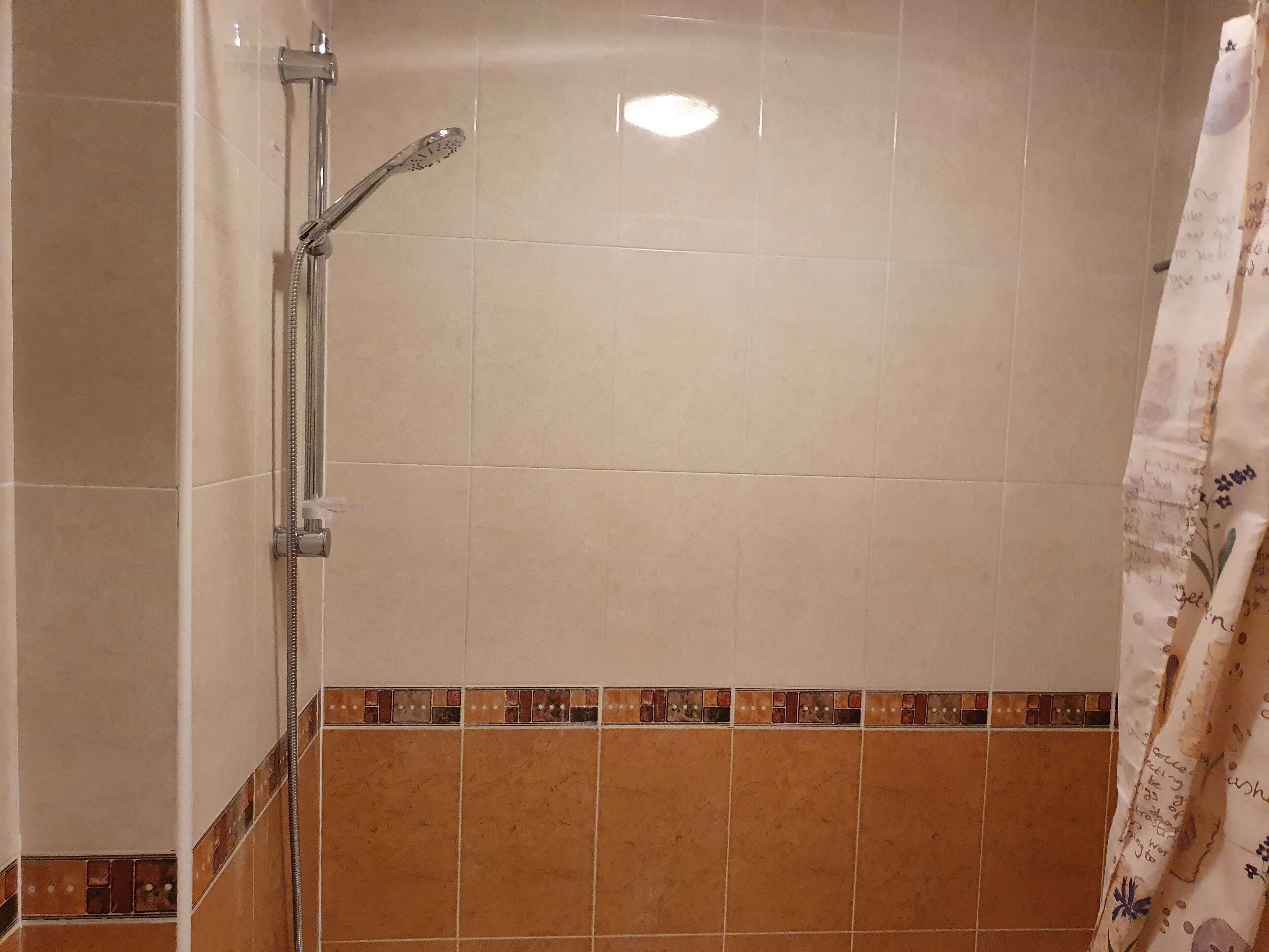 Ein Badezimmer mit beigen und braunen Fliesen, einer Dusche mit Duschbrause und einem Vorhang mit floralem Muster.