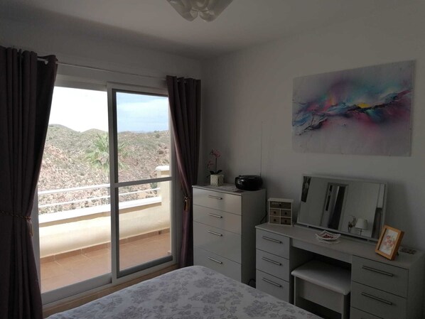 Een slaapkamer met een bed, een bureau, een dressoir, een raam met gordijnen en een schilderij aan de muur.