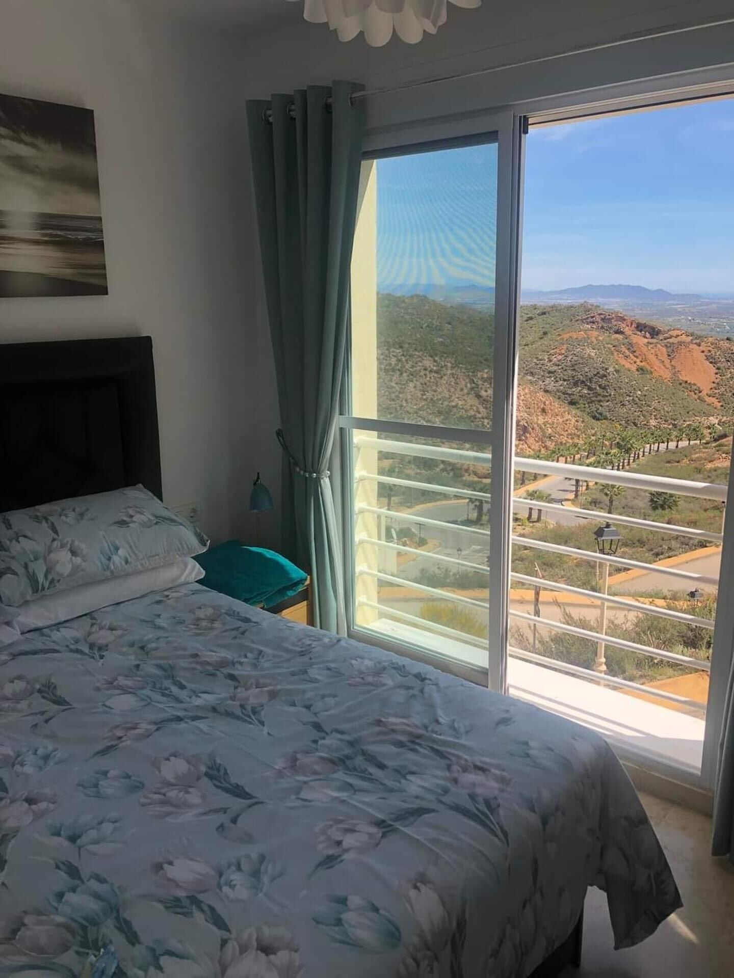 Une chambre à coucher avec un lit, une table de chevet, une fenêtre avec des rideaux et une vue sur un paysage montagneux.