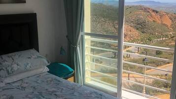 Une chambre à coucher avec un lit, une table de chevet, une fenêtre avec des rideaux et une vue sur un paysage montagneux.