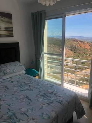 A bedroom with a bed, a nightstand, a window with curtains, and a view of a mountainous landscape. - 2 Bed House Sleeps 4 - Pool, Sea Views, Parking (Bedar)