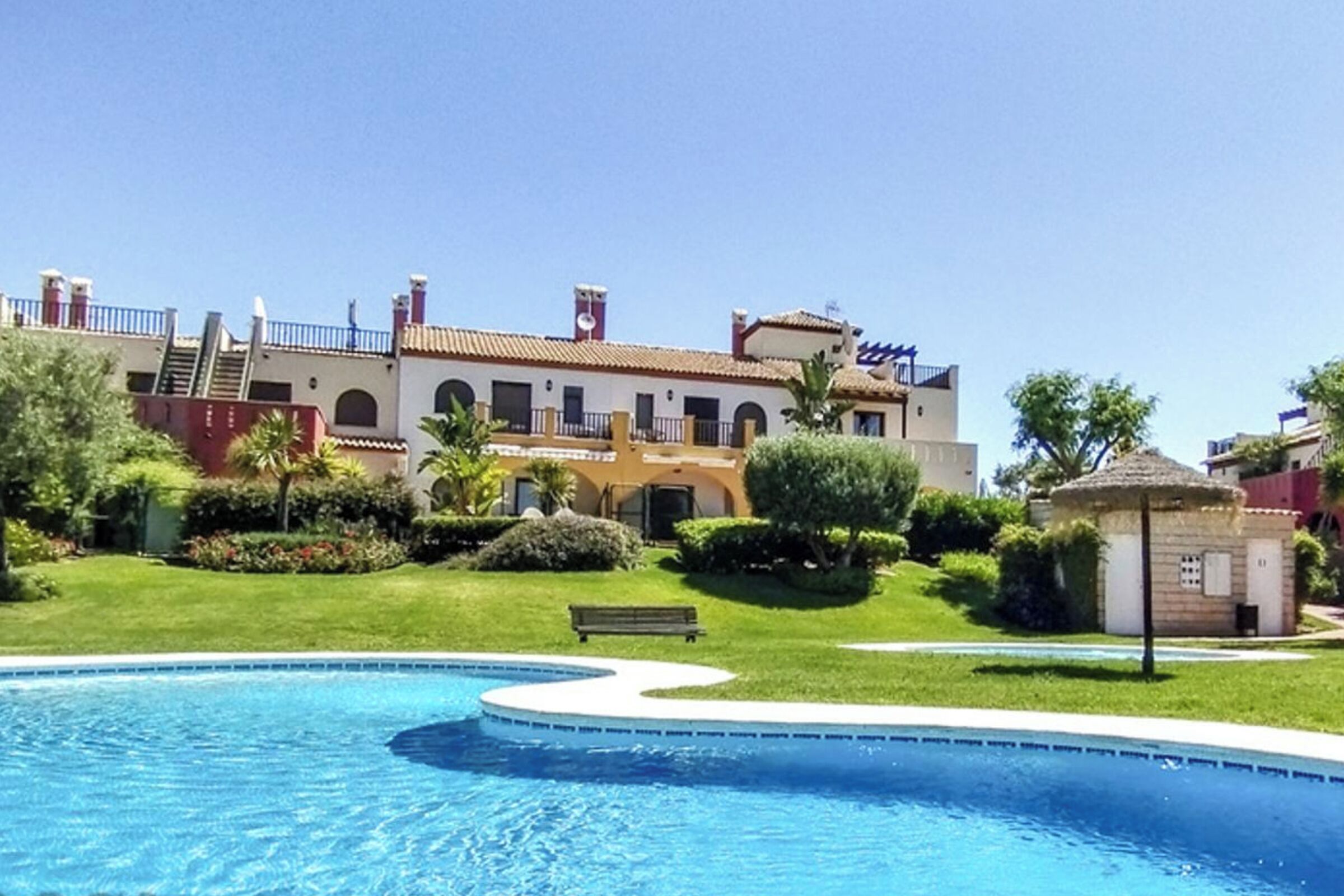Una piscina de borde curvo, rodeada por un césped bien cuidado y un edificio con tejado de azulejos y amplias ventanas.