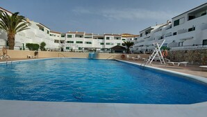 A swimming pool with steps leading into it, surrounded by white buildings with balconies and green shutters. - 1 Bed Apartment - Sleeps 2 - Pool - Parking (Arona)