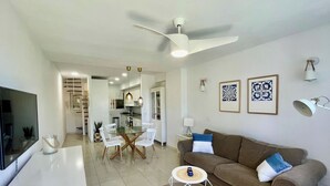 Ein modernes Wohnzimmer mit einem braunen Sofa, einem Glastisch und einem Deckenventilator.