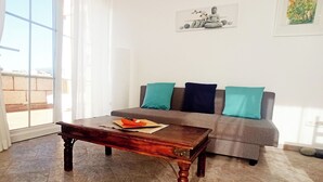 A living room with a wooden coffee table, a grey sofa with teal cushions, and a framed artwork on the wall. - Finca Aurora - Cozy 1-bed Apartment (Arico)
