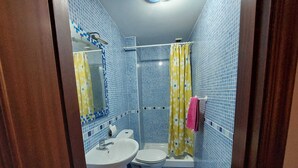 Un bagno con pareti piastrellate di blu, una tenda da doccia gialla, un lavandino bianco e un water.