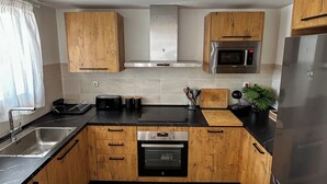 A modern kitchen with wooden cabinets, a stainless steel refrigerator, a microwave, an oven, and a sink. - Green Oasis Costa Casa Adosada con Vistas al Mar (Casares)