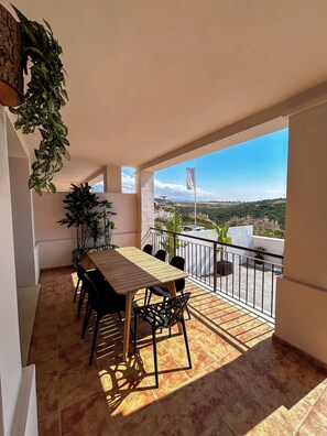 Een balkon met een tafel en stoelen, plantenbakken en een uitzicht op een verafgelegen landschap.