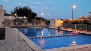 Ein Schwimmbecken mit einer mit Steinplatten belegten Terrasse, umgeben von einem Zaun und Palmen.