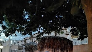 Ein Poolbereich mit blauen Liegestühlen, einem Reedschirm und einer Treppe, die zu einem Kiesstrand führt.