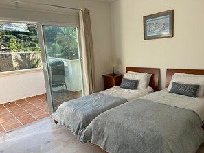 A bedroom with two beds, a balcony with a chair, and a framed picture on the wall. - 3-bed Townhouse, Mijas La Cala Golf & Spa Resort (Mijas)