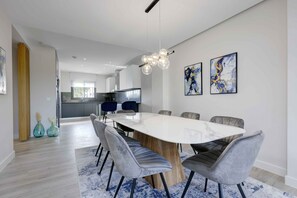 Un comedor moderno con una gran mesa de mármol rodeada de sillas tapizadas en gris, una lámpara colgante contemporánea y arte abstracto en las paredes.