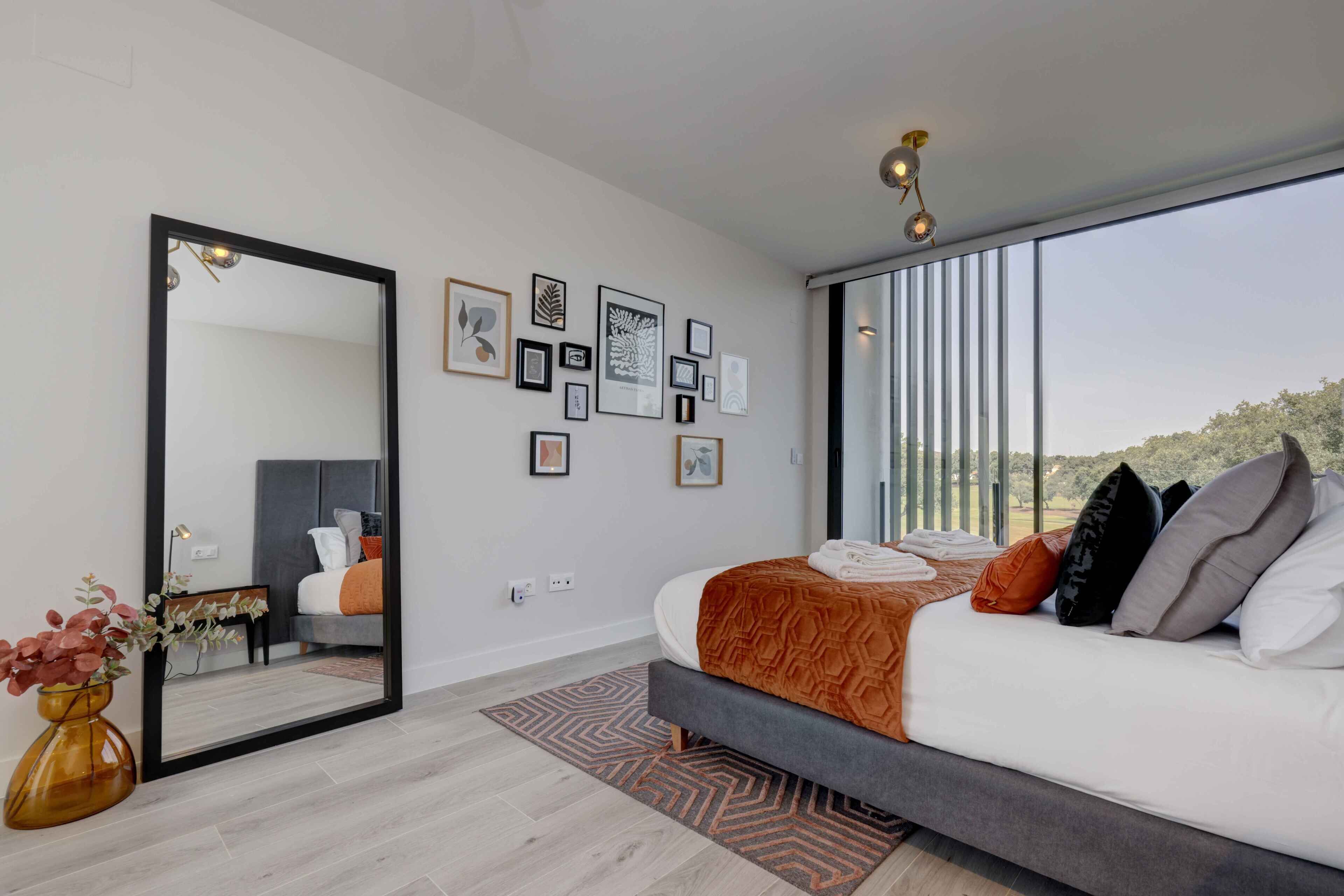 A modern bedroom with a large bed, a mirror, and framed artwork on the wall.