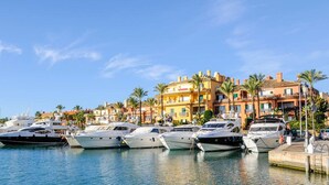 Un puerto deportivo con varios yates amarrados, un paseo marítimo y edificios coloridos al fondo.