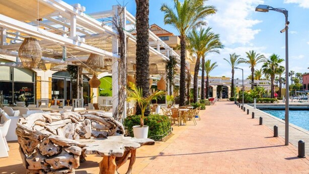 Un resort con mobiliario exterior, palmeras, piscina y un paseo techado.